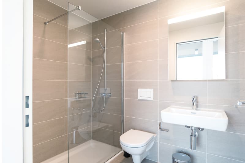 Modern bathroom with beige tile walls, glass shower enclosure, toilet, and sink with vanity