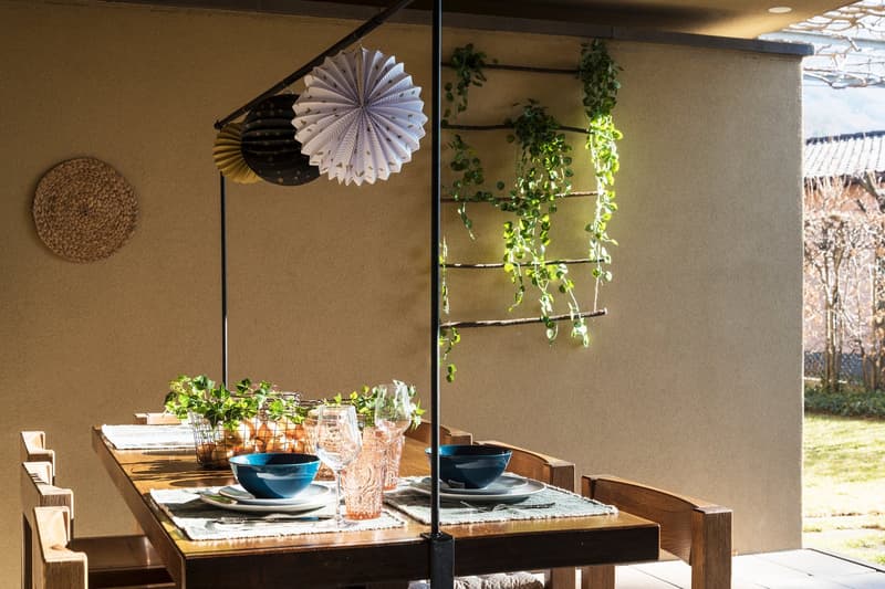 Dining area with wooden table, chairs, and a wall with hanging plants and decorations