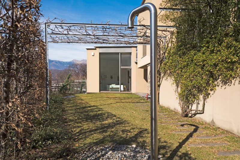 Metal pergola, grassy lawn, metal pole, plants, building with glass doors