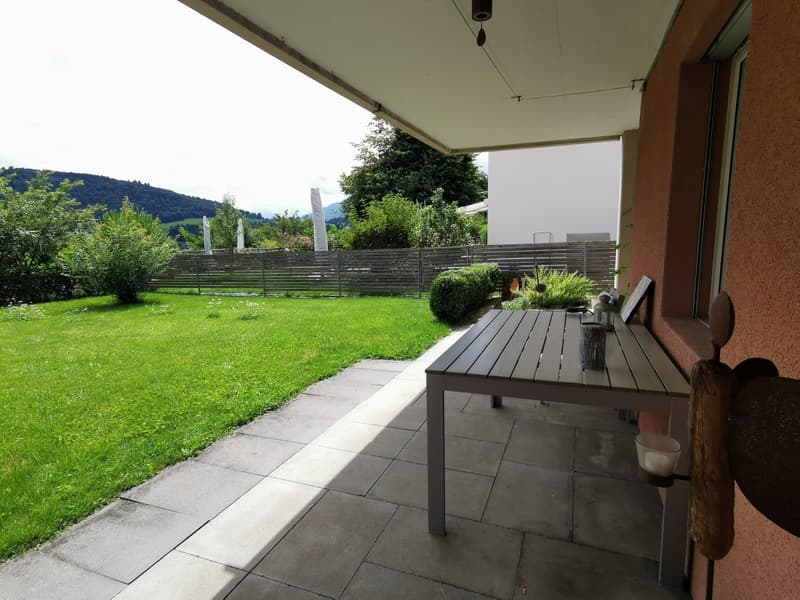 Outdoor patio with table, chairs, and a view of a well-maintained garden and mountains in the distance.