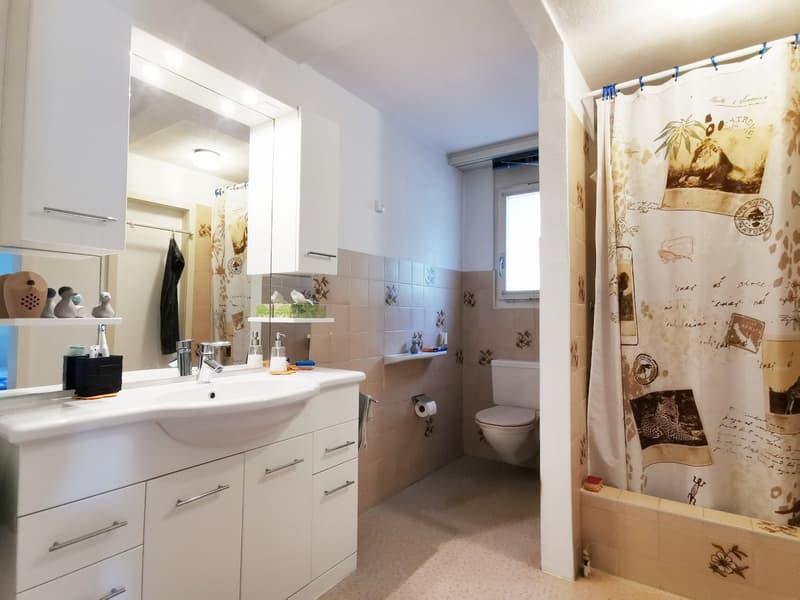 white cabinets, white sink, mirror, shower curtain, toilet, wall tiles, window