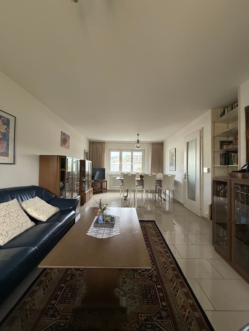 Living room with blue couch, wooden coffee table, TV on a side table, table with chairs, dining area