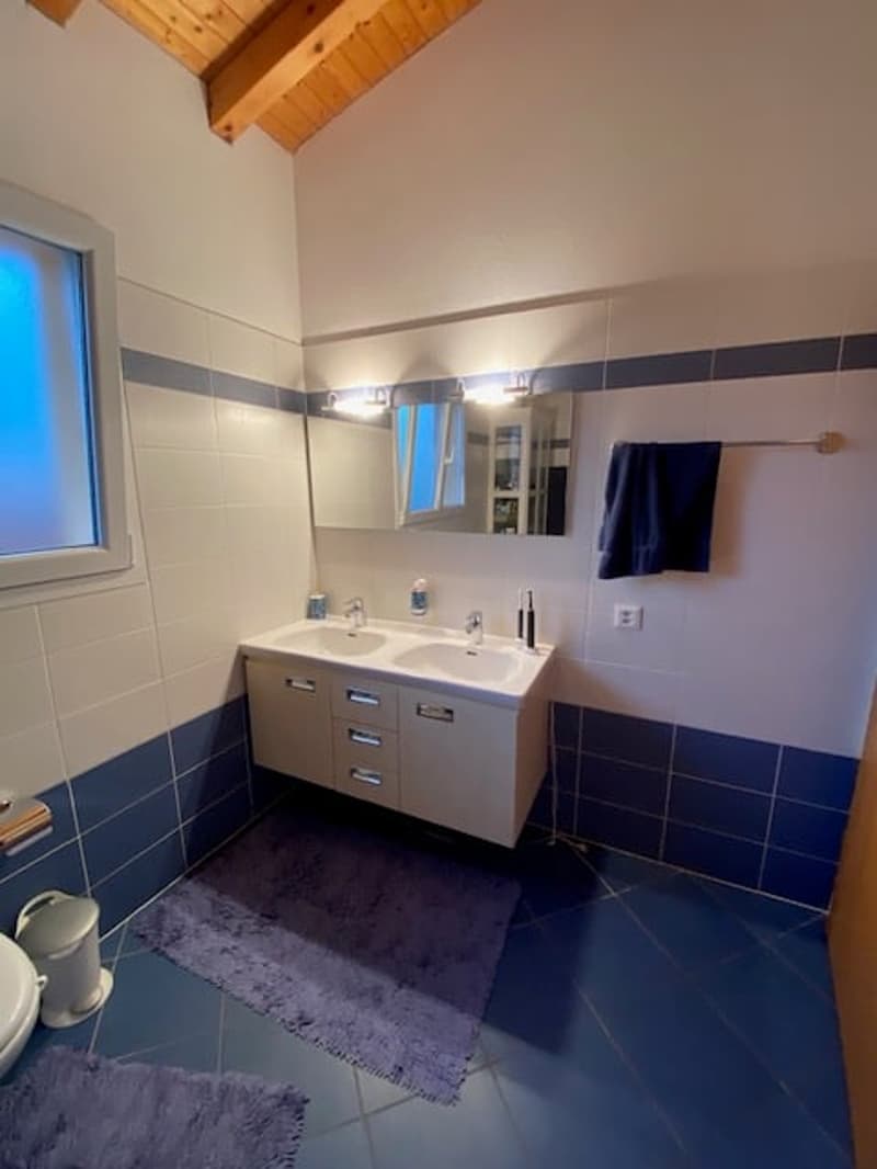 modern bathroom with blue and white tiles, double vanity with two sinks, a mirror, and wooden ceiling