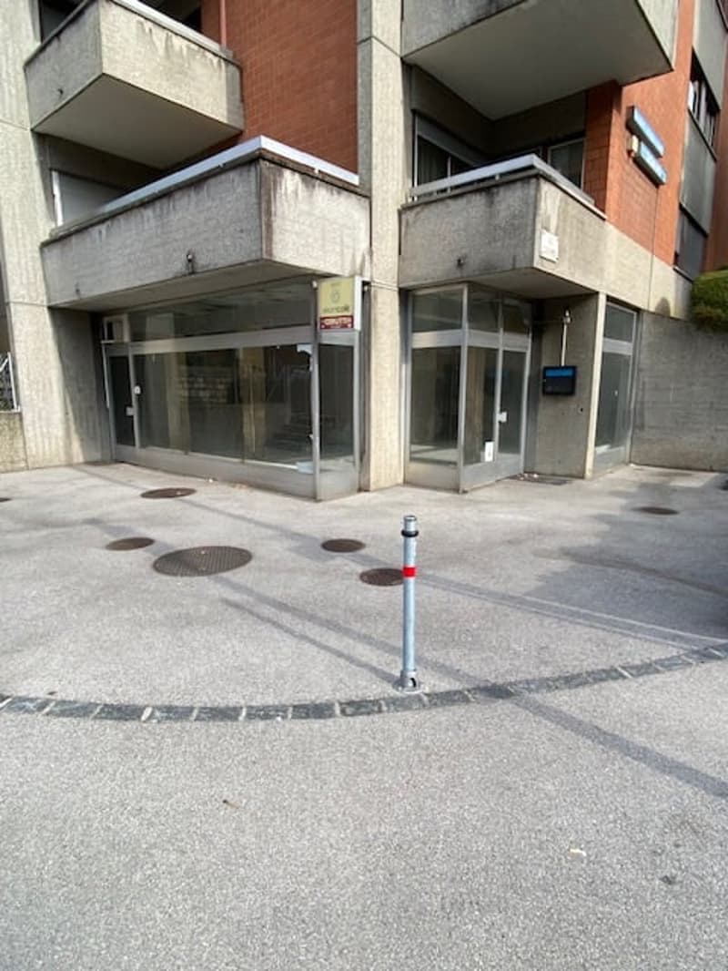 Facade of a building with glass doors, metal grates, and a parking area with visible poles.