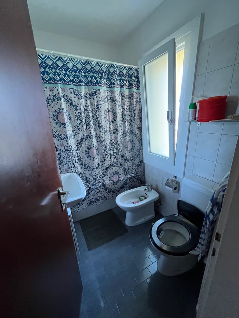white toilet, bidet, sink, blue shower curtain, open window