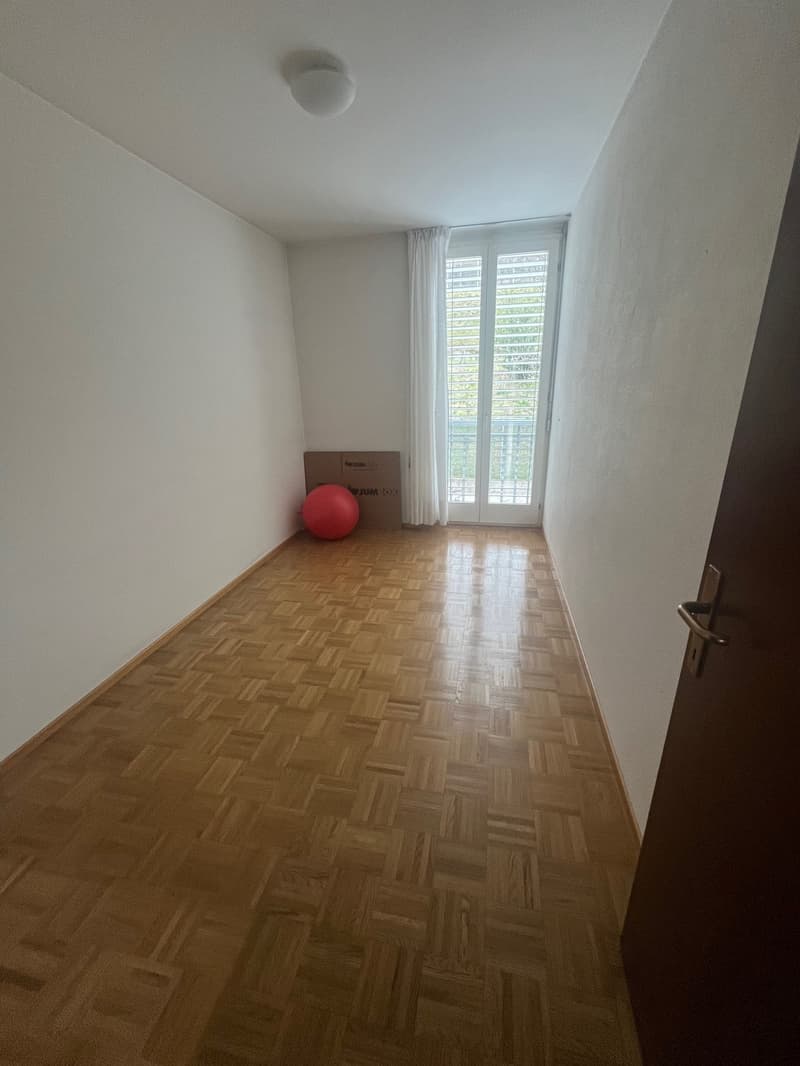 empty room with balcony, wooden floor, white walls, white curtains, red exercise ball, cardboard box