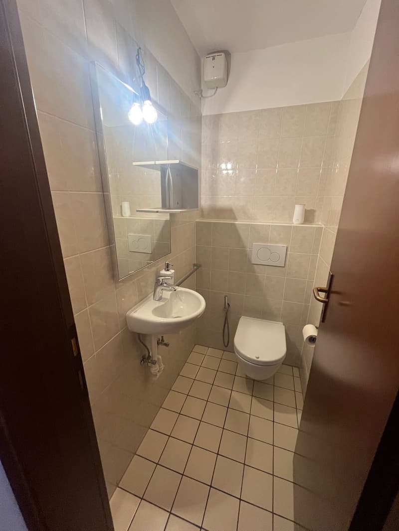 small bathroom with white tiles, white sink, mirror, toilet, no window