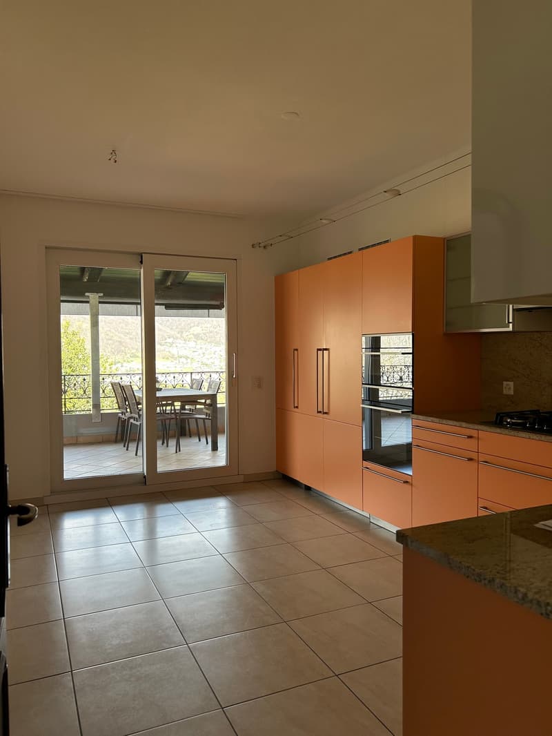 Spacious open-plan kitchen with orange cabinets, granite countertops, and sliding glass doors leading to a balcony or terrace with a view of the outdoors.