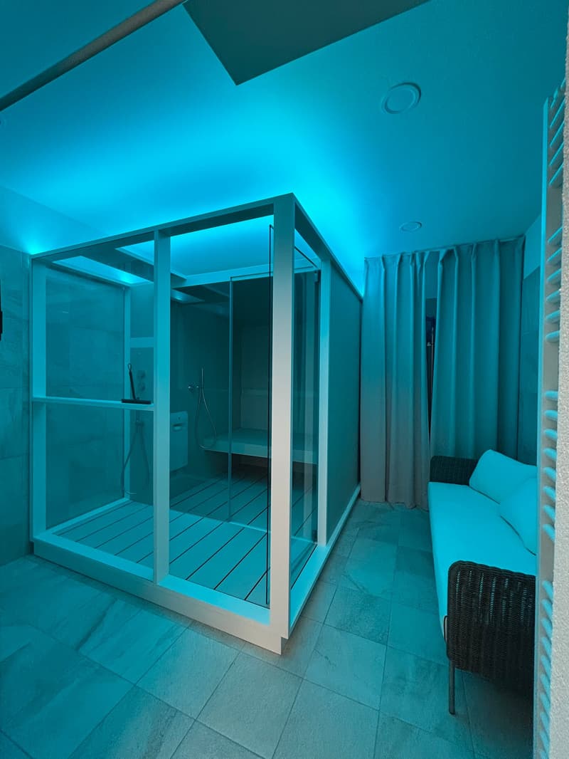 Glass-enclosed room with blue lighting, tiled floor, and a wicker chair