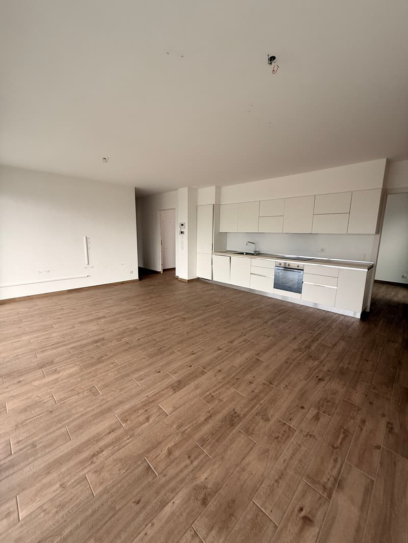 empty room with modern kitchen setup, white cabinets, wooden floor, a door leading to another room