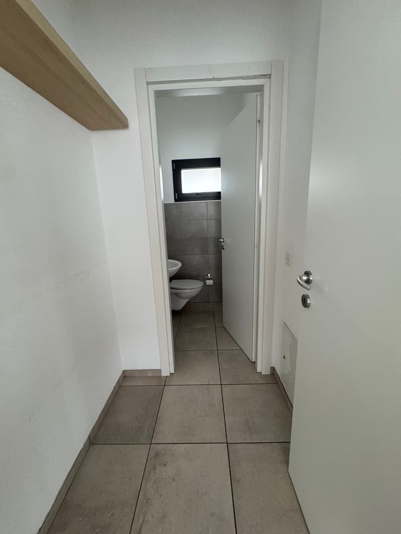 Empty bathroom with white walls, tiled floor, toilet, sink, and a window