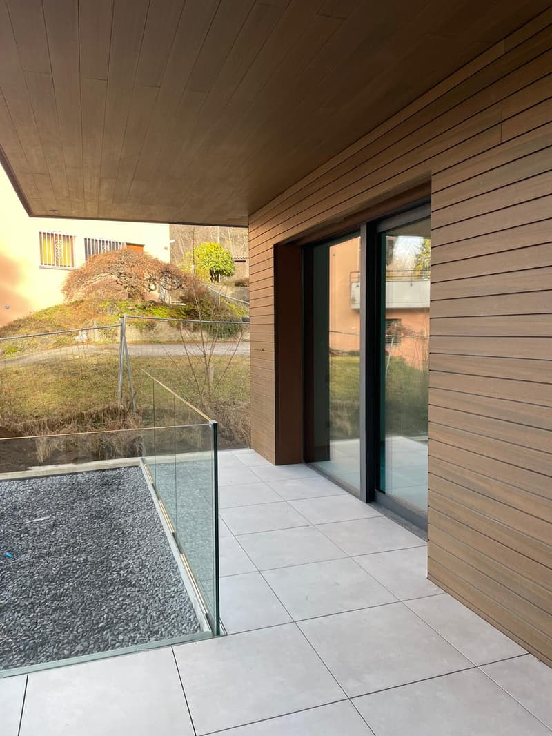 covered terrace with glass railing, tiled floor, metal railing, wooden wall, large window