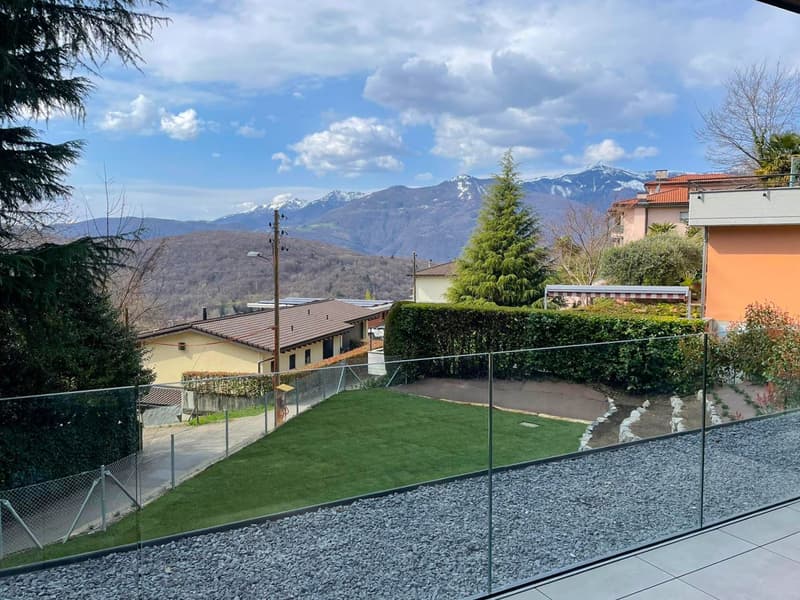 View of a garden with gravel path, green lawn, hedges, and mountains in the background