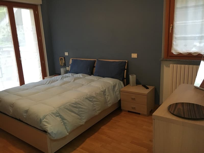 Double bed with white and blue bedding, two bedside tables with lamps, wooden floor, and a window with curtains