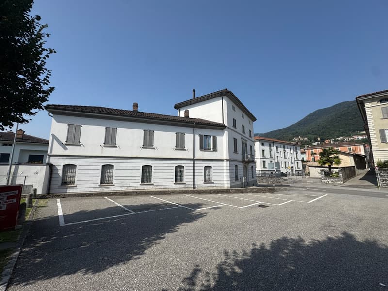 white building, multiple windows, brown roof, parking lot in front