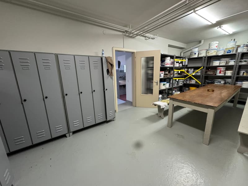 an empty storage room with gray metal lockers, a table, a shelf with containers, and a bench