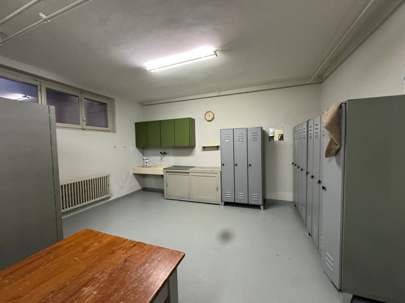 Empty room with lockers, sink, and a table, and windows.
