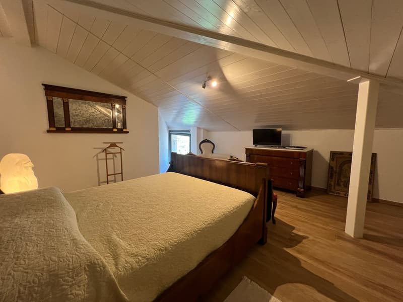 Bedroom with wooden bed, wooden floor, white walls, wooden cabinet, TV, mirror, lamp, and chair