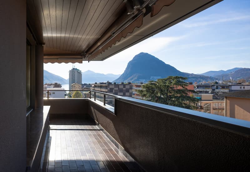 Balcony with tiled floor, metal railing, and a view of mountains and buildings