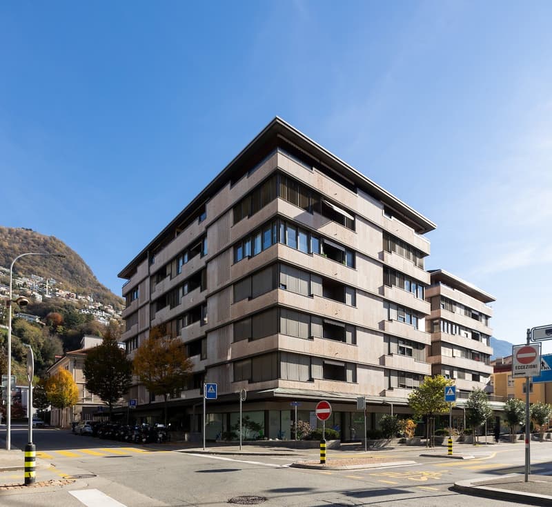 Multi-story building, concrete exterior, multiple windows, ground floor with commercial space, street level parking