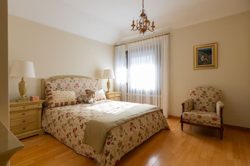 A bedroom with a bed, nightstands, a chair, a chandelier, and a picture frame on the wall