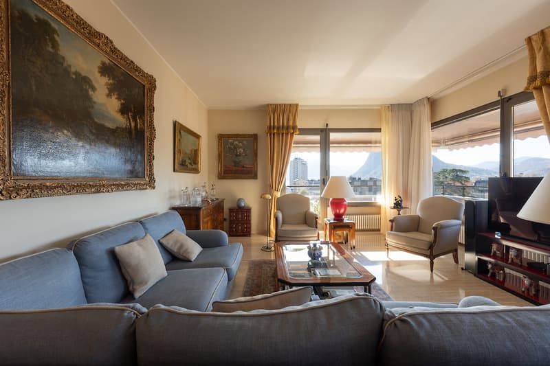 living room with large windows, blue sofa, coffee table, two armchairs, paintings, radiator, TV, lamp