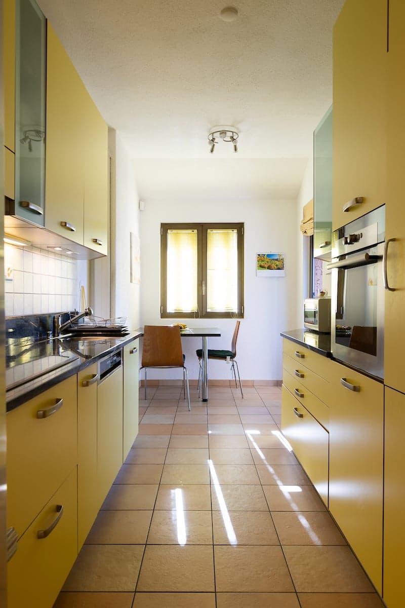 modern kitchen with yellow cabinets, tiled floor, stainless steel appliances, sink, faucet, dining table with chairs, window with blinds, microwave, oven