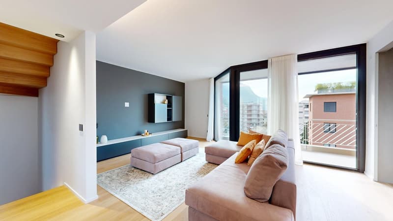 Spacious living room with large windows, hardwood floors, gray accent wall, built-in TV unit, comfortable sofa and armchair, and a balcony with a view