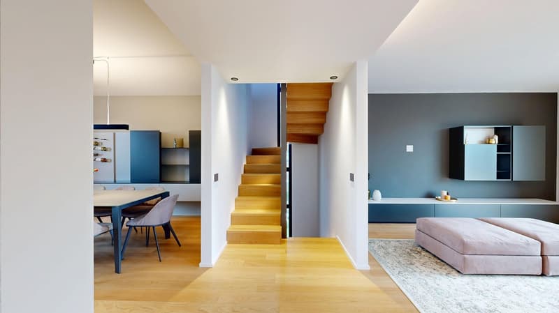 Open-concept living space with wooden stairs, blue and white built-in cabinets, dining table, and a cozy seating area with a pink sofa.