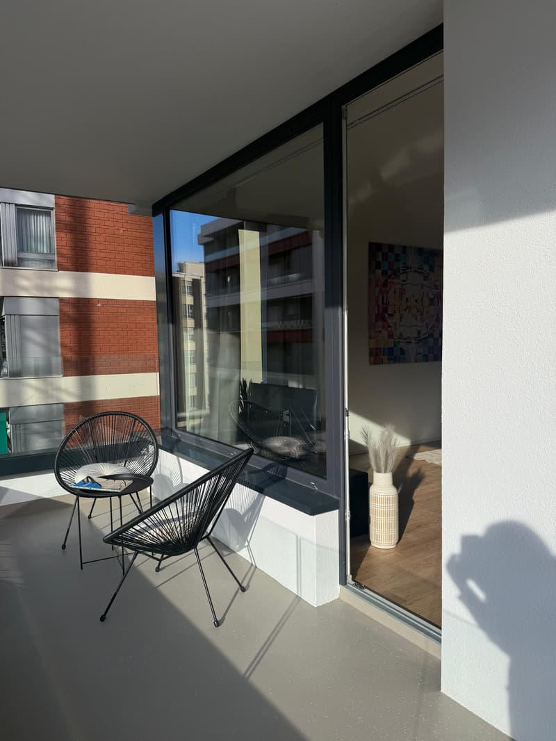 a balcony with chairs, a table, and a view of the buildings