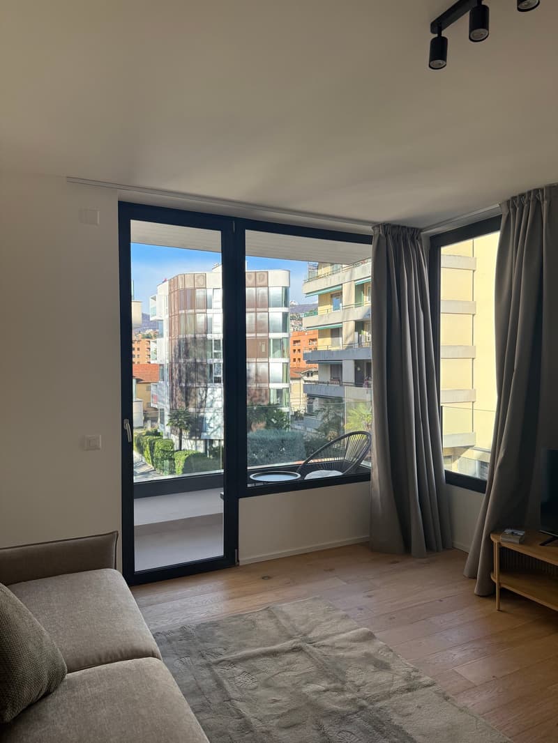glass sliding doors, sofa, hardwood floor, coffee table, balcony, window curtains, view of the city