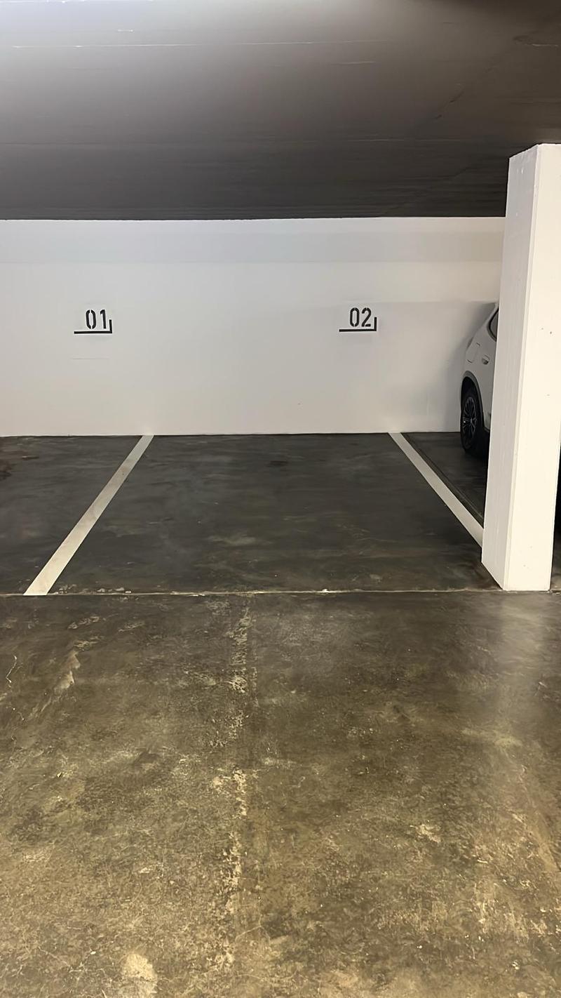 Underground parking lot with two parking spaces, white walls, grey floor, and white pillars