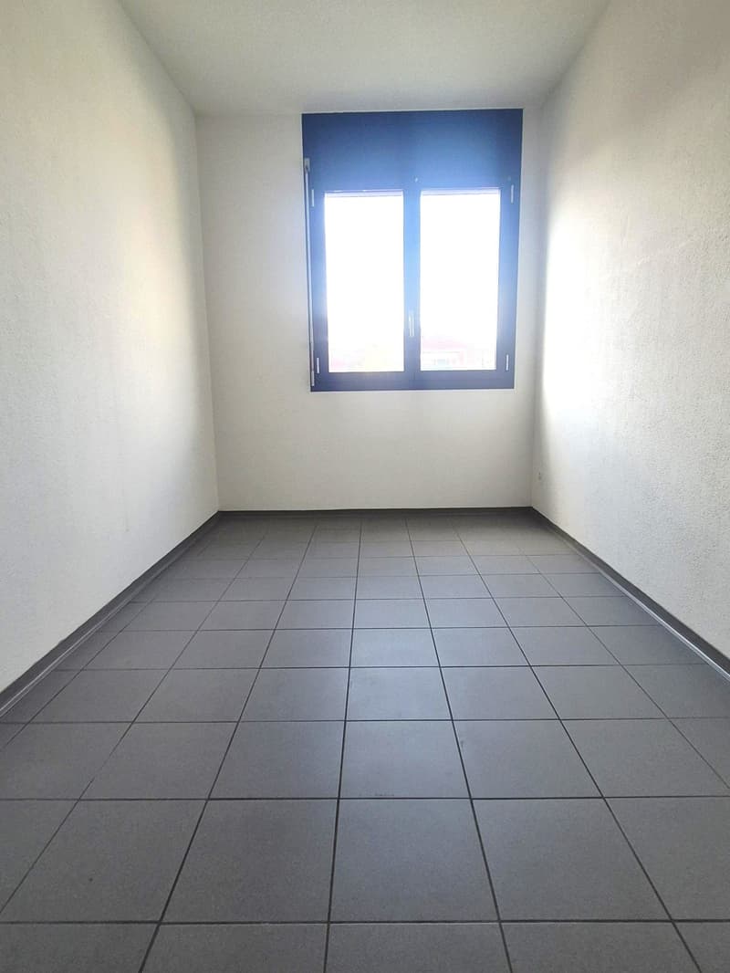 Empty room with white walls, gray tiled floor, single window