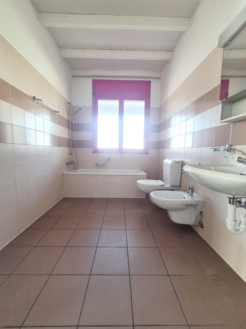 bathroom with bathtub, two toilets, sink, tiled floor, tiled walls, window