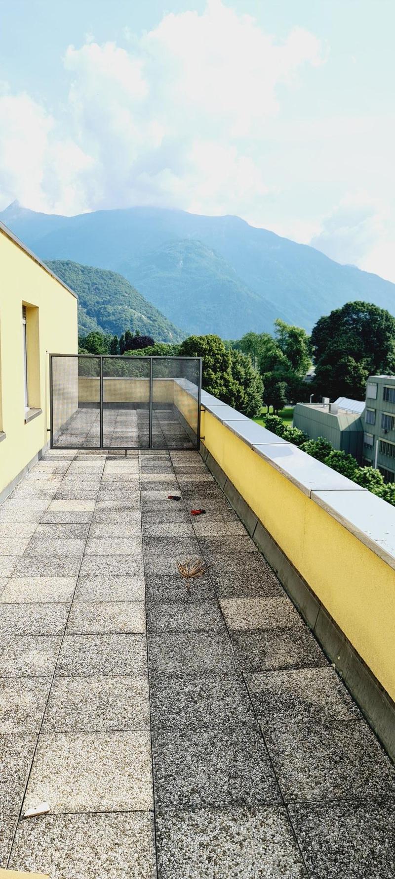 balcony terrace with yellow wall and gravel floor, metal railing, mountains in the distance