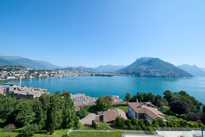 House with a view of the lake and mountains, surrounded by trees and greenery
