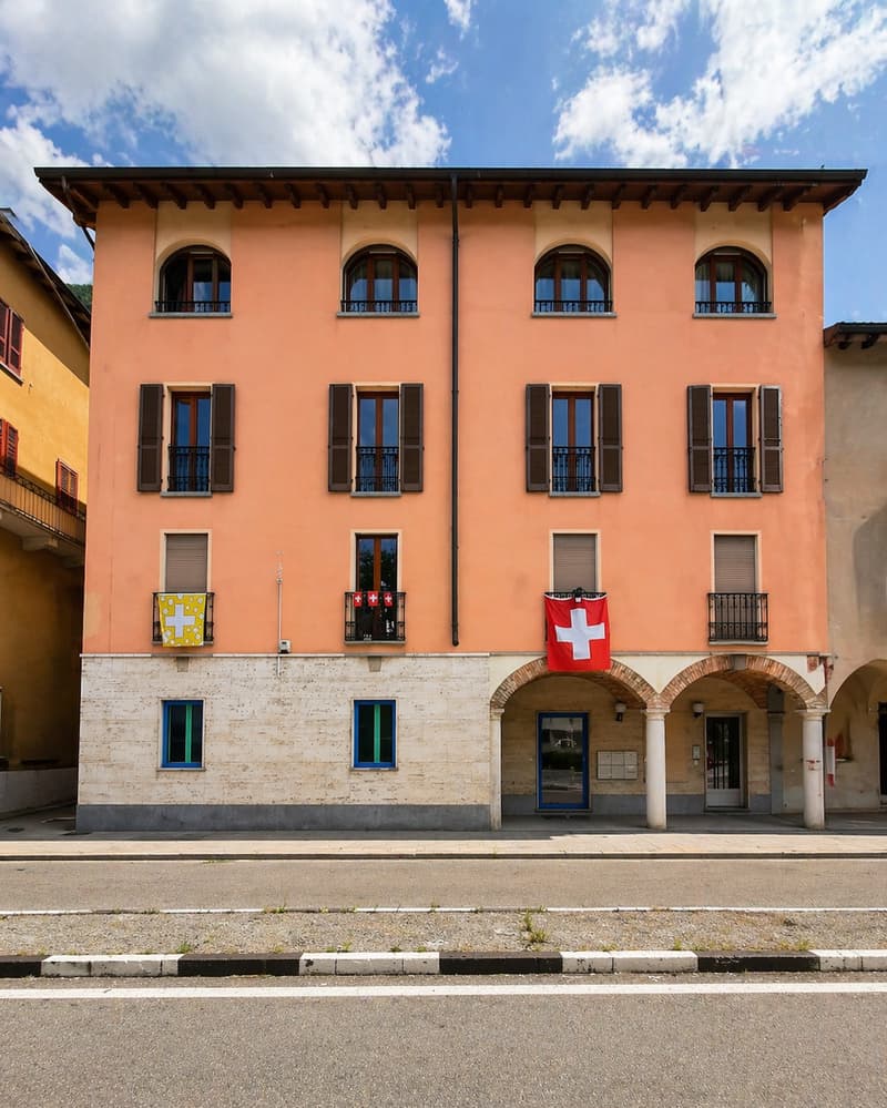 Three story building, beige and orange walls, multiple windows, Swiss flag on the front