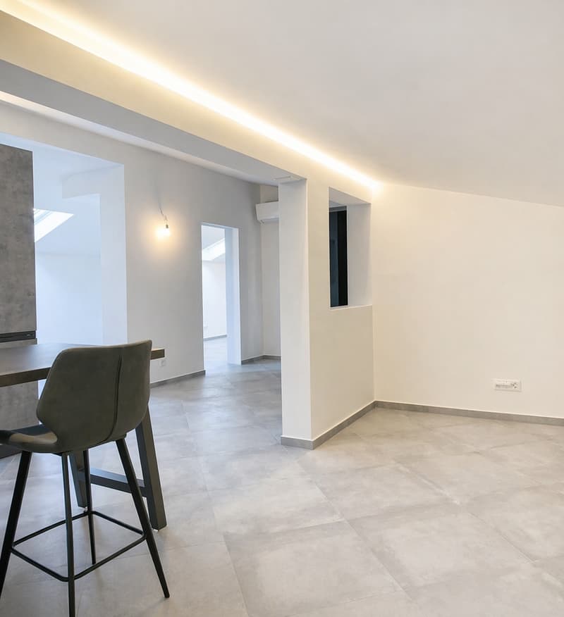 Empty room with white walls, gray floor, a table with a chair, a ceiling light, and an air conditioner