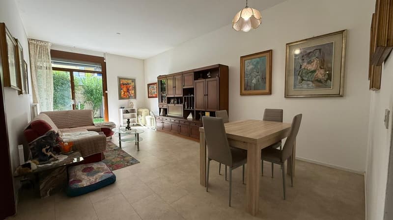 Large room with couch, wooden table, dining chairs, bookshelf, glass door, windows, framed paintings