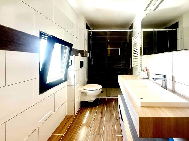 modern bathroom with white tiles, wooden floor, double sink, toilet, shower, window