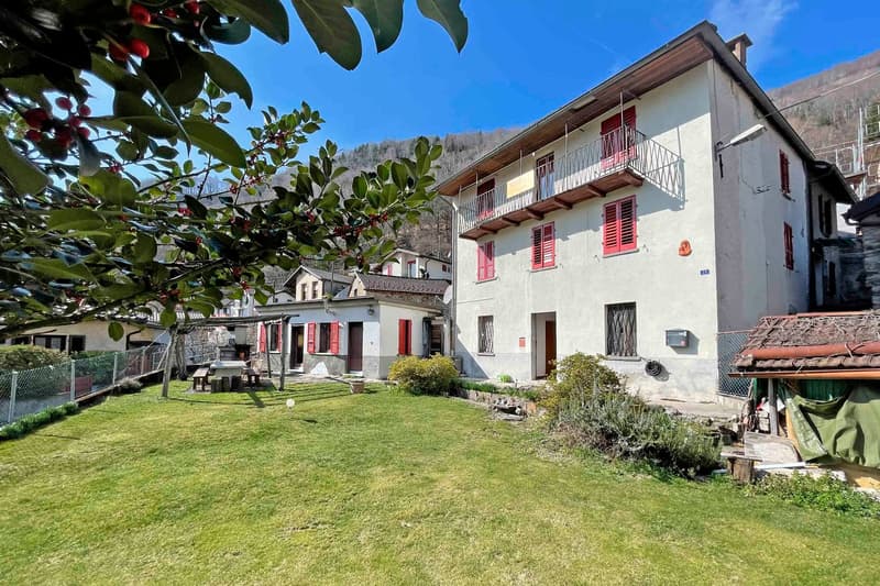 2 story building, white walls, red shutters, balcony, mountain in the background, fence, lawn, patio