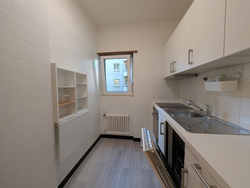 Open kitchen, tiled walls, wooden floor, integrated appliances, white cabinetry, stainless steel sink, and faucet