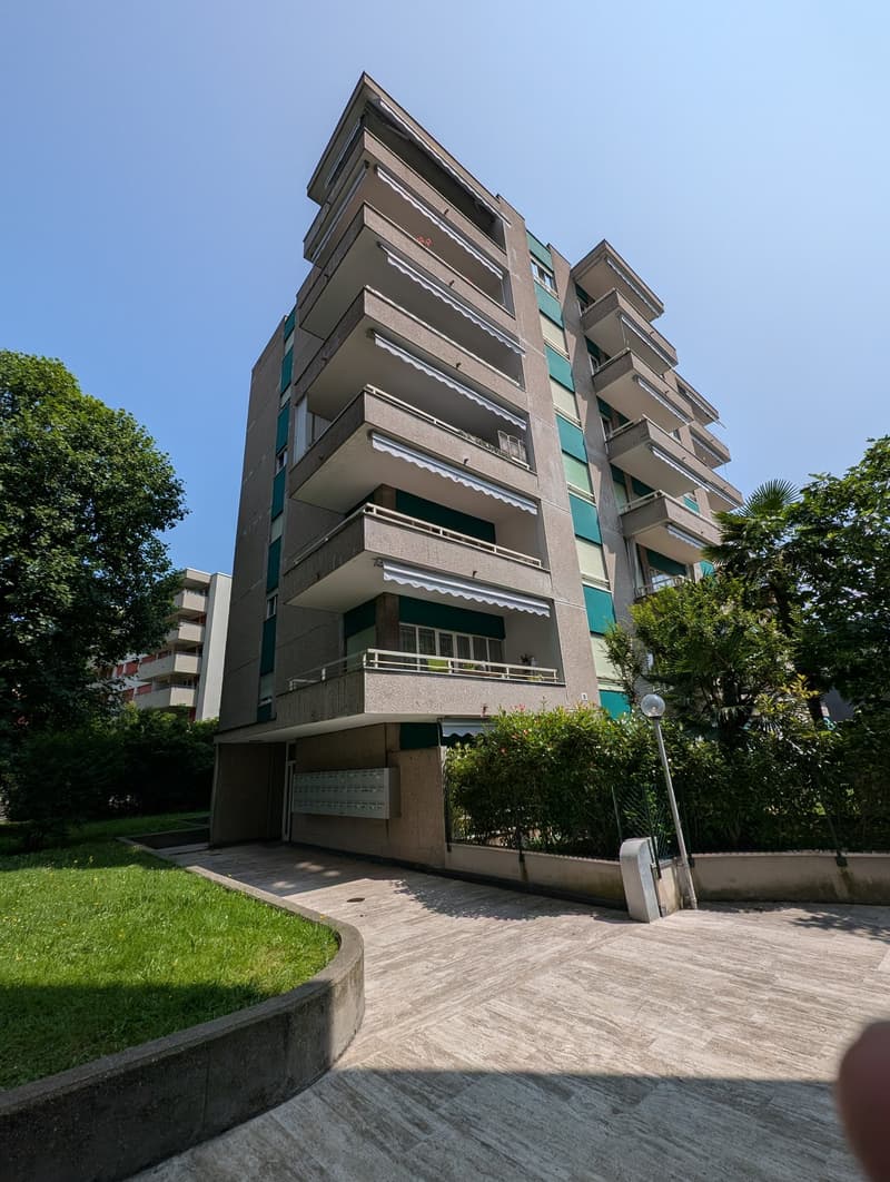 7-story apartment building, green and beige exterior, multiple balconies, driveway, green grass lawn
