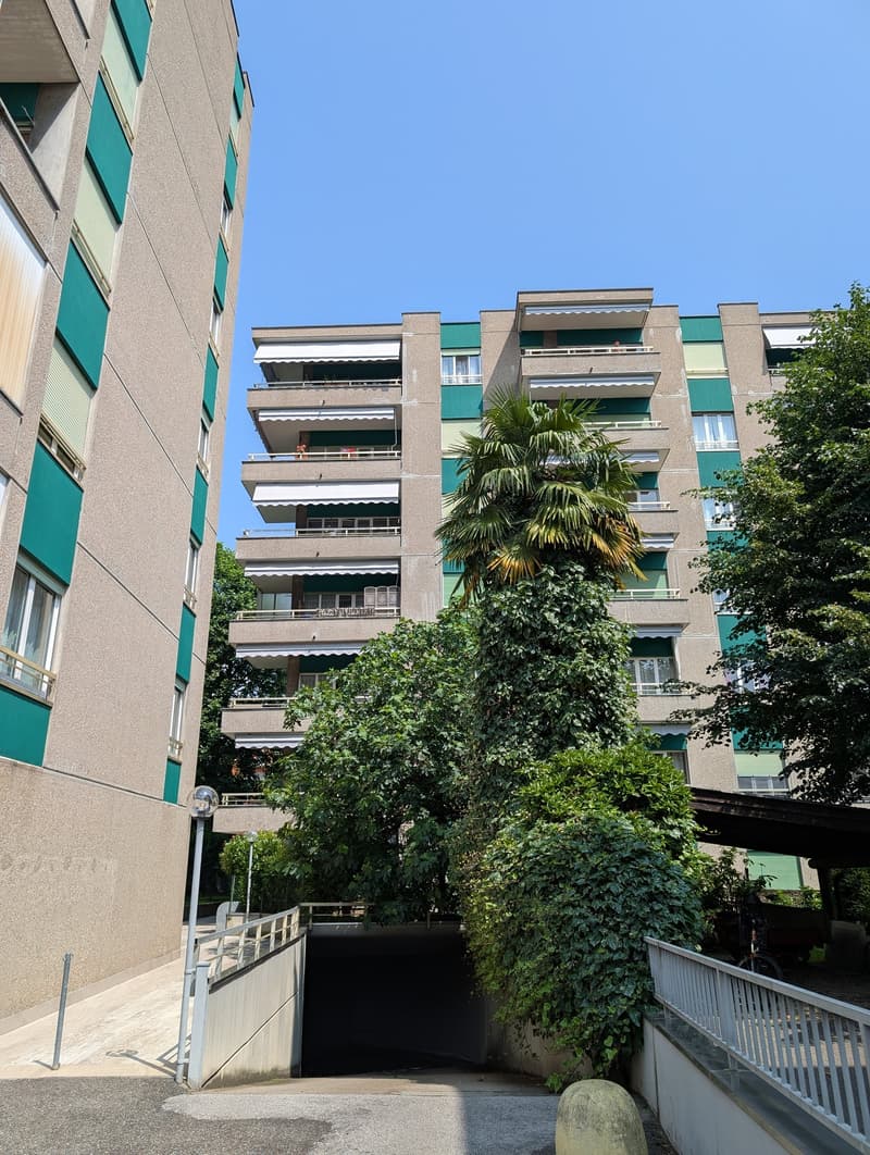 A modern, multi-story building with multiple balconies, windows, and a garage entrance.