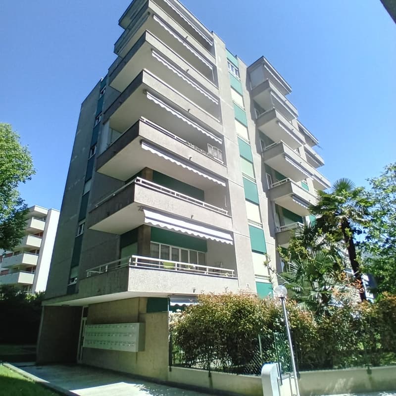 Multi-storey residential building, green facade, balconies with railings, entrance area, front yard with greenery