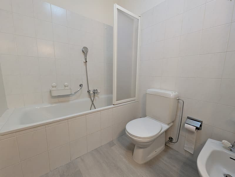 Bathroom with white tiled walls, bathtub, shower, toilet, sink