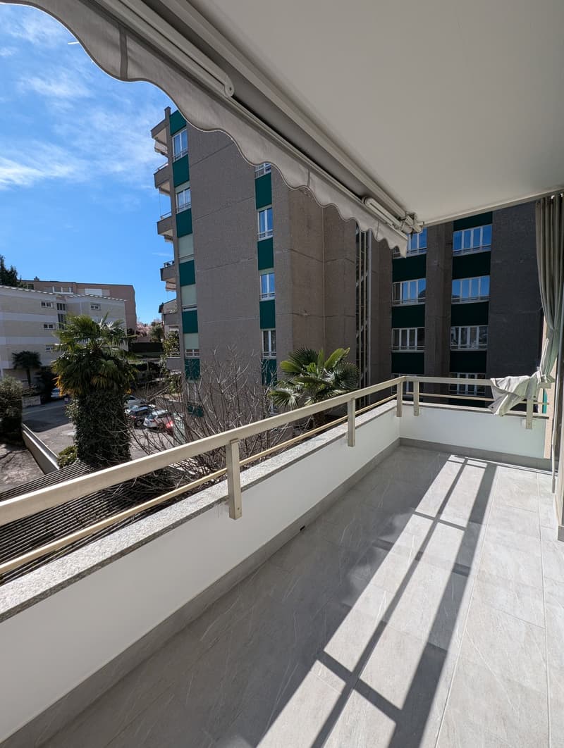 large balcony with tiled floor, metal railing, awning, view of the street and buildings