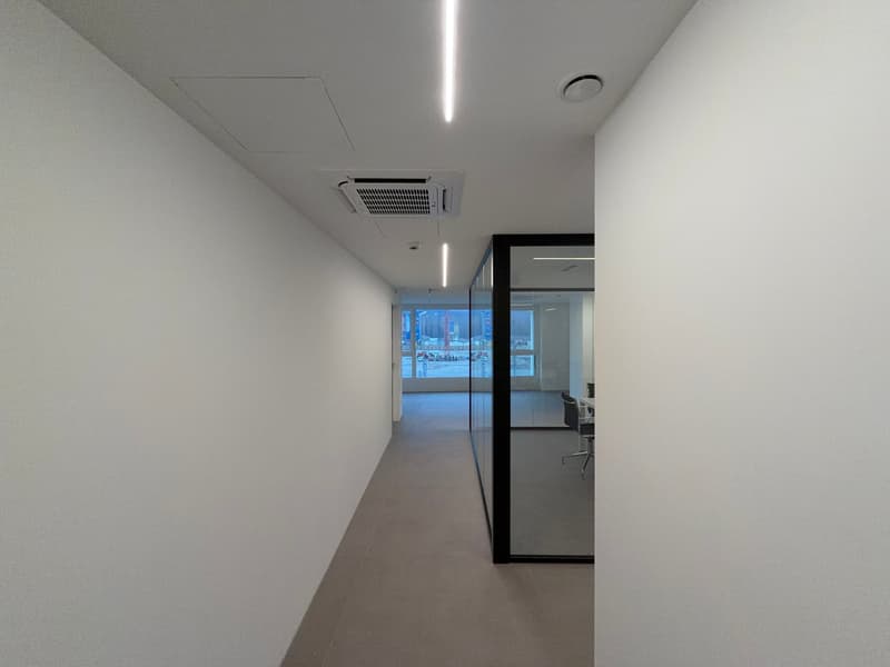 Empty room with plain white walls, gray floor, glass partition, visible window