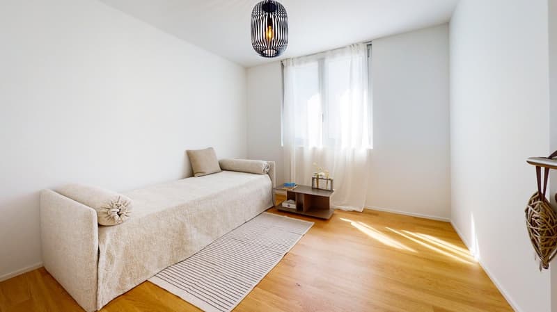 A small daybed with pillows, a rug, a small table, and a window with white curtains