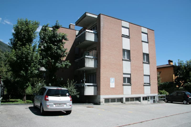 Multistory building, red bricks, several windows, balconies, parking in front